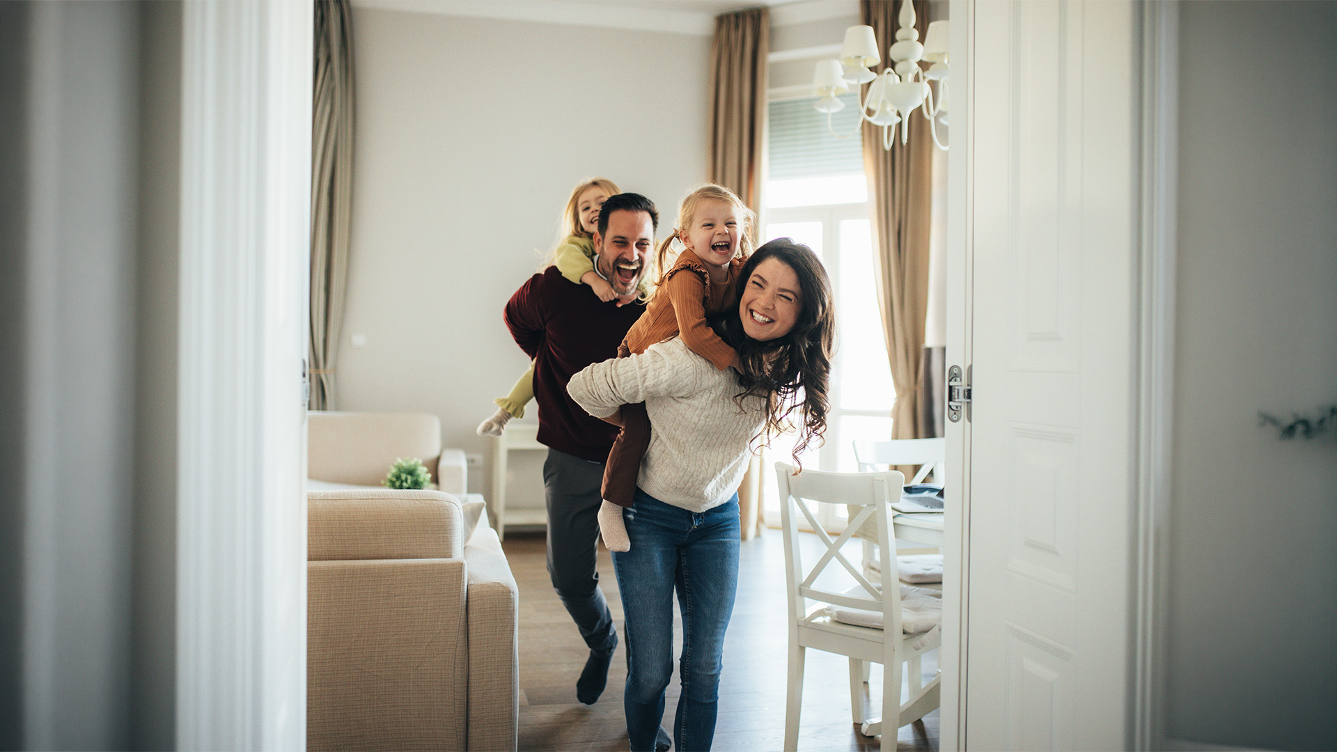 Smiling family enjoying quality time together with parents giving their children piggyback rides in their home